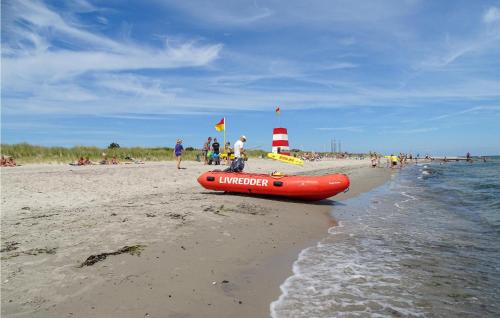 a red boat on a beach with people and a lighthouse at Holiday Home Aspevej Grenaa Iv in Grenå