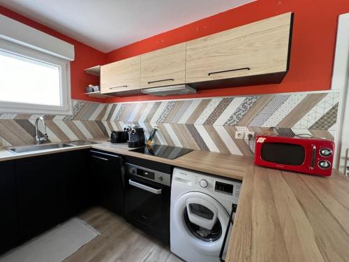 - une cuisine équipée d'un lave-linge et d'un four micro-ondes rouge dans l'établissement Jolie maison paisible, à Gujan-Mestras