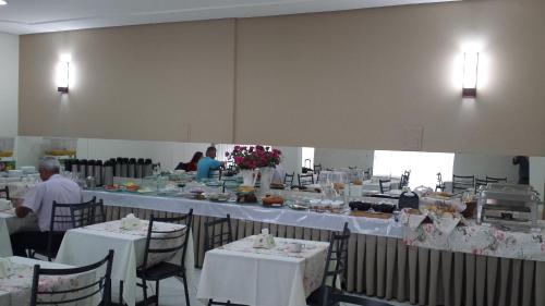 a dining room with white tables and chairs and people at Hotel Pouso Novo in Matão