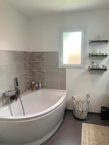 La salle de bains est pourvue d'une baignoire blanche et d'une fenêtre. dans l'établissement Jolie maison contemporaine avec piscine, à Saint-Jean-dʼIllac