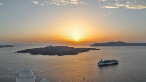 a boat in the water with the sunset in the background at Aroma Suites in Fira