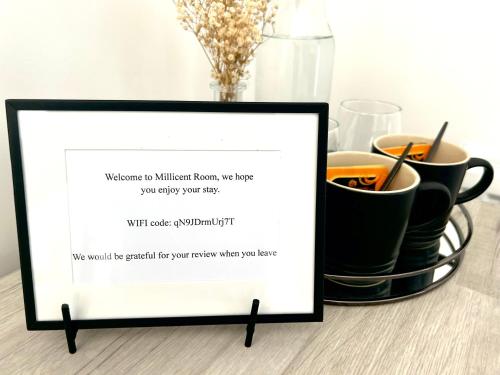 a framed sign sitting on a table with coffee cups at Millicent Room in Littlehampton