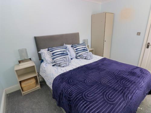 a bedroom with a bed with a purple comforter and pillows at Bluebell Cottage in Cardiff