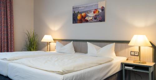 a bedroom with a white bed with two lamps at Hotel Kreuzer in Wedel