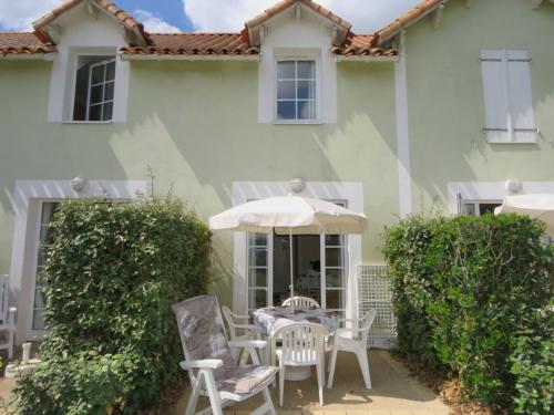 une terrasse avec des chaises et un parasol en face d'une maison dans l'établissement Maison résidence accès piscine gratuite, à Talmont-Saint-Hilaire