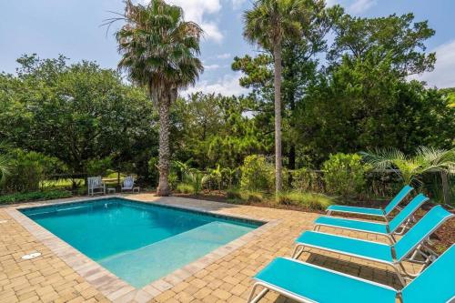 a swimming pool with two blue chairs and palm trees at Pompano Pool House in Edisto Island