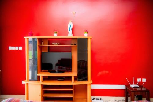a room with a red wall with a tv on a shelf at Fleur Guest House in Kigali