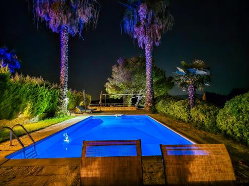 a pool with two chairs and palm trees at night at Villa Palma Posidi with Private pool in Kalandra