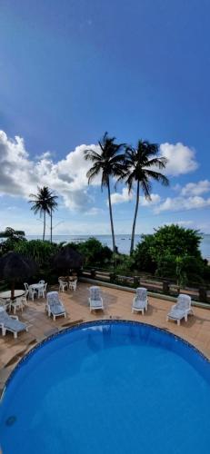 a swimming pool with white chairs and palm trees at Pousada dos Veleiros in Nova Almeida
