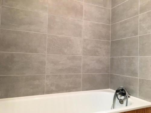 La salle de bains est pourvue d'une baignoire blanche et d'un mur en carrelage gris. dans l'établissement Résidence Etoile - Studio pour 2 Personnes 524, à La Plagne Tarentaise