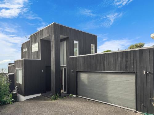 a black house with two garage doors at Murrays Gem l Modern 4bed Stunner l Sea View & Spa! in Auckland