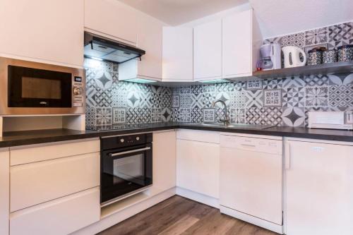 une cuisine avec des armoires blanches et des appareils noirs dans l'établissement Résidence Plein Soleil - Appartement 2 pièces 6 personnes Plagne Villages MAE-4484, à La Plagne Tarentaise