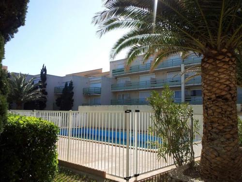 une clôture blanche avec un palmier devant un bâtiment dans l'établissement Appartement RDC avec Terrasse dans residence avec piscine et face à la plage, à Leucate