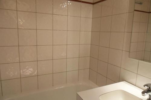 La salle de bains est pourvue de carrelage blanc, d'une baignoire et d'un lavabo. dans l'établissement Résidence Corail - Studio pour 4 Personnes 044, à Aime La Plagne