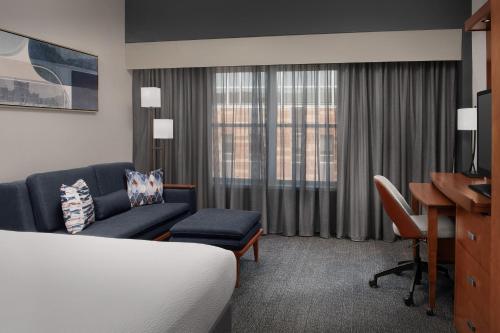 a hotel room with a bed and a couch and a desk at Courtyard Syracuse Downtown at Armory Square in Syracuse