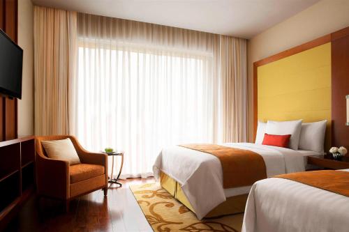 a hotel room with two beds and a chair and a window at Courtyard by Marriott Kochi Airport in Nedumbassery
