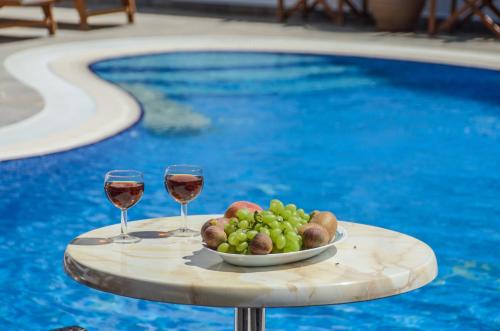 a plate of grapes and wine glasses on a table next to a pool at Orama Apartments in Agia Anna Naxos