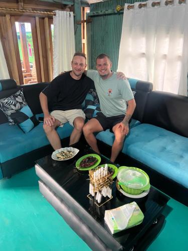 two men sitting on a couch with food on a table at Jhuna Komodo Homestay in Komodo