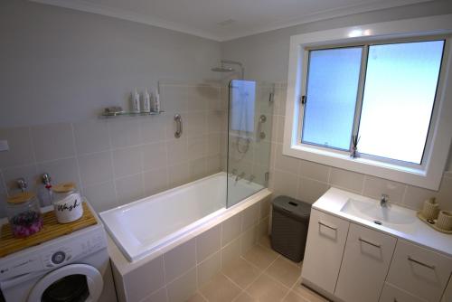 a bathroom with a tub and a sink and a washing machine at Ella's Beach Haven in Batehaven