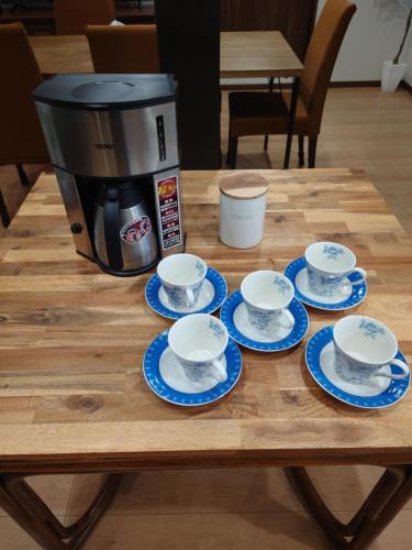 a coffee maker and four cups and saucers on a table at ゲストハウス　風の丘 in Aji