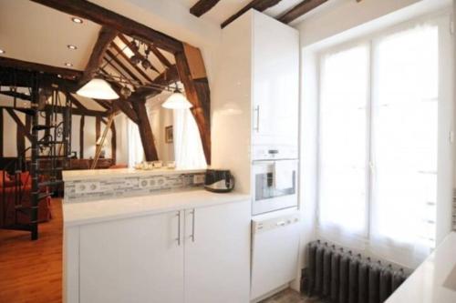 une cuisine avec des placards blancs et une grande fenêtre dans l'établissement Duplex Paris proche du Panthéon, à Paris