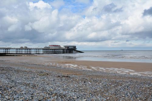 a beach with a pier in the background with a rocky shore at The Fabulous Number Two Apartment a cosy coastal getaway in Cromer