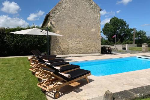 - un ensemble de chaises longues avec un parasol à côté de la piscine dans l'établissement Le Pressoir de la Vieville, Gite Renoir, à Mandeville-en-Bessin