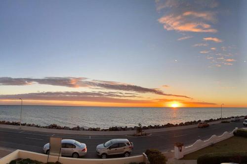 a road with cars parked next to the ocean at sunset at entire beachfront apartment 5 Esplanades seaviews in Glenelg