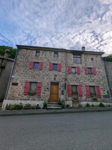 un vieux bâtiment en pierre avec des volets rouges et une porte dans l'établissement Le lys de la vallée, à  Labastide-sur-Bésorgues