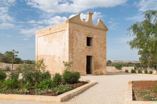 an old brick building in the middle of a garden at Masseria Donna Menga - The Leading Hotels of the World in Torre Lapillo