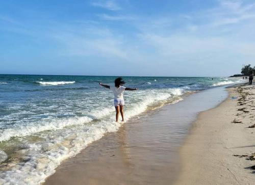 a woman walking on the beach near the ocean at Diani 2BR Coastal Villa - 4 Mins To The Beach in Diani Beach