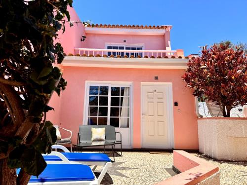 a pink house with blue chairs and a door at Falesia Gardens in Caniço