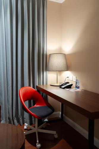 a red chair sitting next to a desk with a lamp at Swiss-Belcourt Serpong in Ciater-tengah