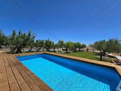 a blue swimming pool with a wooden deck and trees at Trulli Nannì in Locorotondo
