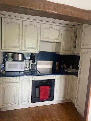 - une cuisine avec des placards blancs et une serviette rouge sur un four dans l'établissement Au coeur de l'Aveyron, à Montagnol