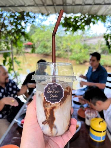 a hand holding a cup of coffee with a straw at HatYai -Les Cat Cocoa Farmstay in Ban Tha Mo Chai