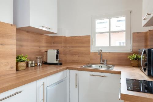 une cuisine avec des armoires blanches, un évier et une fenêtre dans l'établissement Appartement 75017 proche Champs Elysées, à Paris