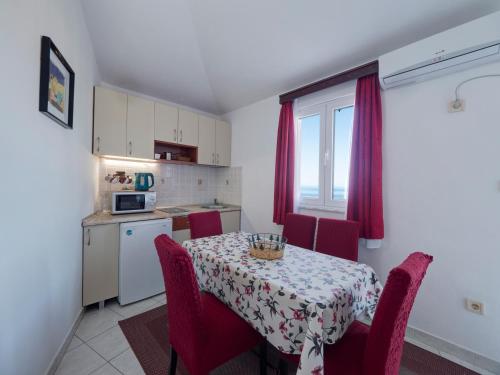 a dining room table with red chairs and a kitchen at Apartments Marina in Sveti Stefan