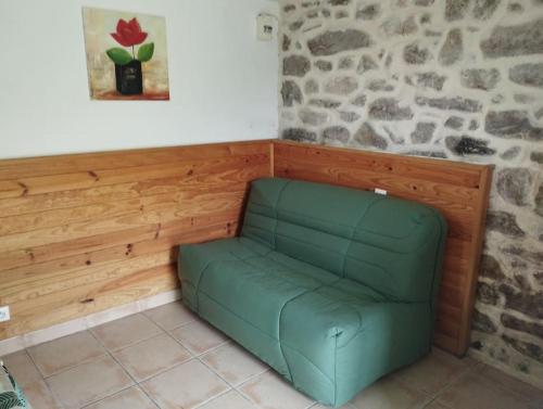 a green couch in a room with a stone wall at Cascade - Gîte pour 2 personnes in La Salvetat