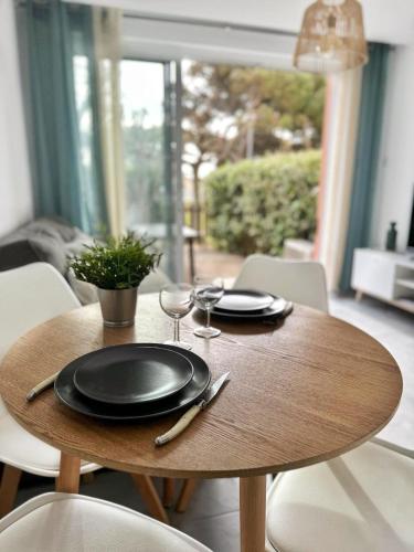 une table en bois avec des assiettes et des verres à vin dessus dans l'établissement Appartement 4 personnes, Piscine, Parking à Palavas les flots, à Palavas-les-Flots