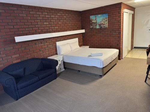 a bedroom with a bed and a chair in a brick wall at Mid City Plantation Motel in Mildura