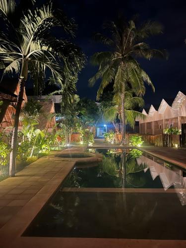 a resort with a pond and palm trees at night at Living Trawangan Hotel in Gili Trawangan