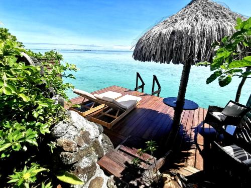 a deck with chairs and an umbrella and the ocean at Hôtel Fenua Mata'i'oa in Papetoai