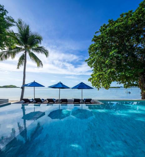 a swimming pool with umbrellas and chairs and the ocean at Homm Chura Samui in Chaweng