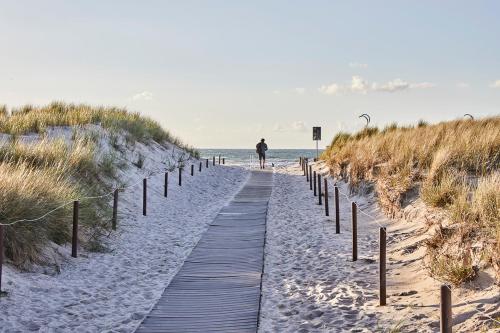 a person walking down a wooden path to the beach at Baltic Hideaways Beach Hotel Warnemünde in Warnemünde