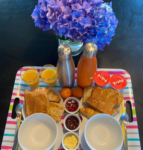 a tray with toast bread and orange juice and a vase of flowers at La Chambre de Claire in Les Iffs