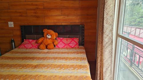 a teddy bear sitting on a bed with red pillows at AK Homestay in Dehradun