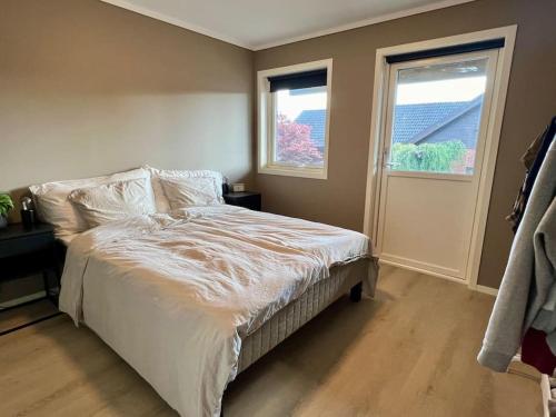 1 dormitorio con 1 cama con sábanas blancas y 2 ventanas en Bo moderne på Falkum med utsikt, en Skien