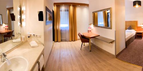 a hotel room with a bathroom with a bed and a desk at City Hotel Ost am Kö in Augsburg