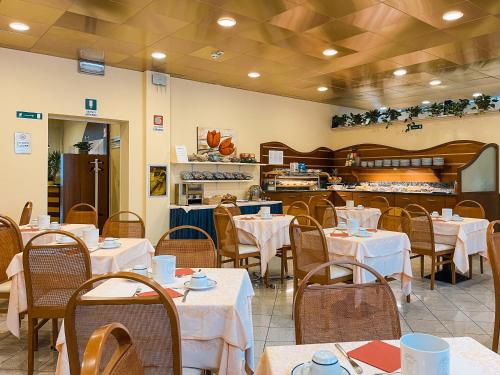 a restaurant with white tables and chairs and a kitchen at Aparthotel Pineda in Bibione